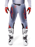 Alpinestars 2025 Supertech Lipan broek, motorcrossbroek, grijs en neonoranje, gedragen met rood-zwarte handschoenen en wit-zwarte laarzen, met grote Alpinestars-sterlogo's op de dijen en ventilatieperforaties voor professioneel racen