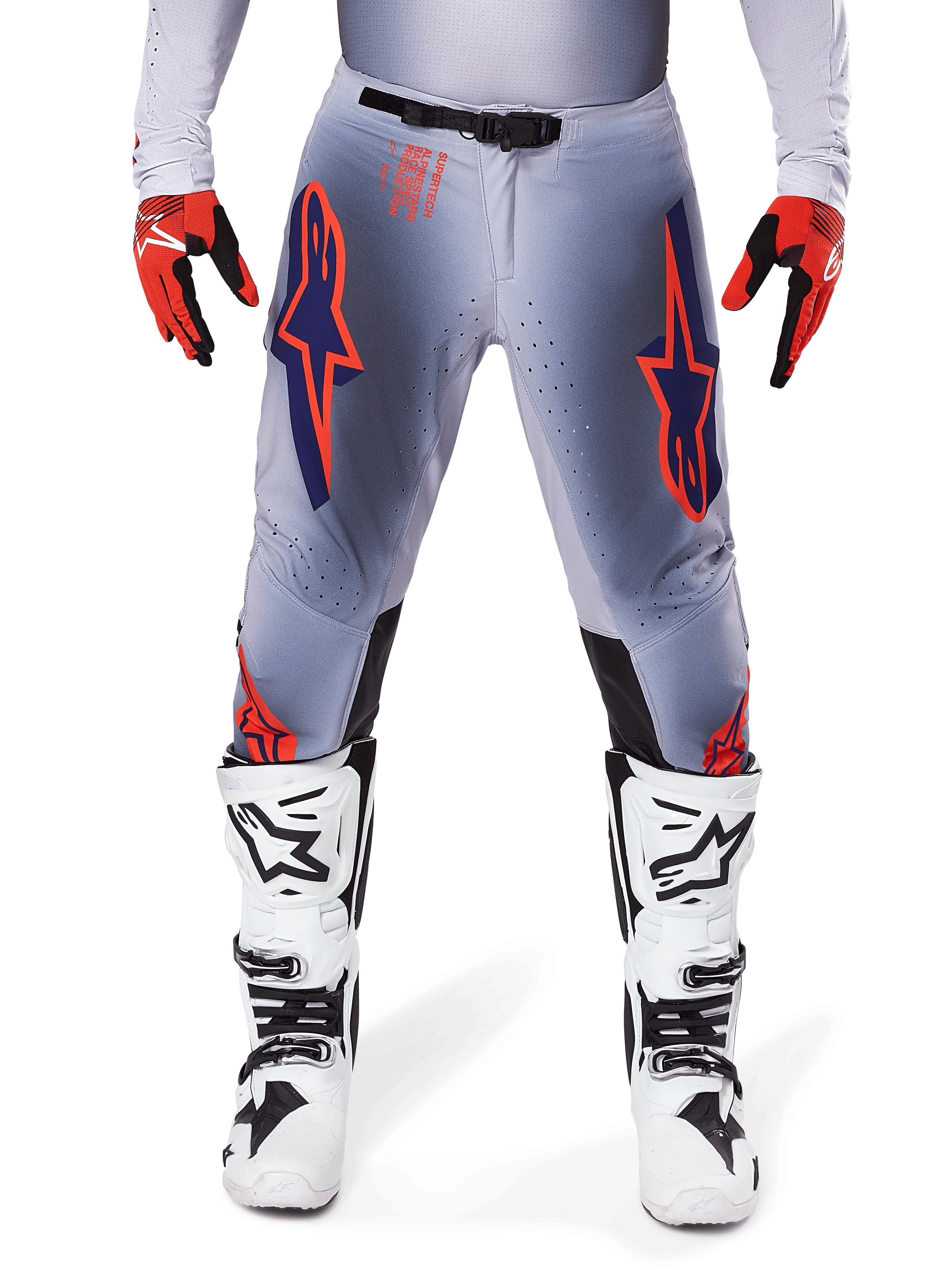 Alpinestars 2025 Supertech Lipan broek, motorcrossbroek, grijs en neonoranje, gedragen met rood-zwarte handschoenen en wit-zwarte laarzen, met grote Alpinestars-sterlogo's op de dijen en ventilatieperforaties voor professioneel racen