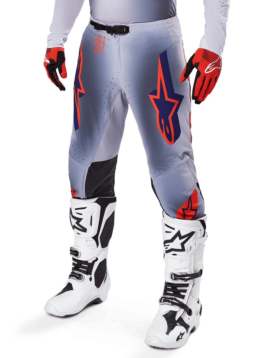 Alpinestars 2025 Supertech Lipan broek, motorcrossbroek, grijs en fluoriserend oranje, met donkerblauwe sterren en zwarte binnenkniepanelen, gedragen met roodoranje handschoenen en witte laarzen, professionele off-road race-uitrusting