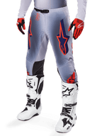Alpinestars 2025 Supertech Lipan broek, motorcrossbroek, grijs en fluoriserend oranje, met donkerblauwe sterren en zwarte binnenkniepanelen, gedragen met roodoranje handschoenen en witte laarzen, professionele off-road race-uitrusting