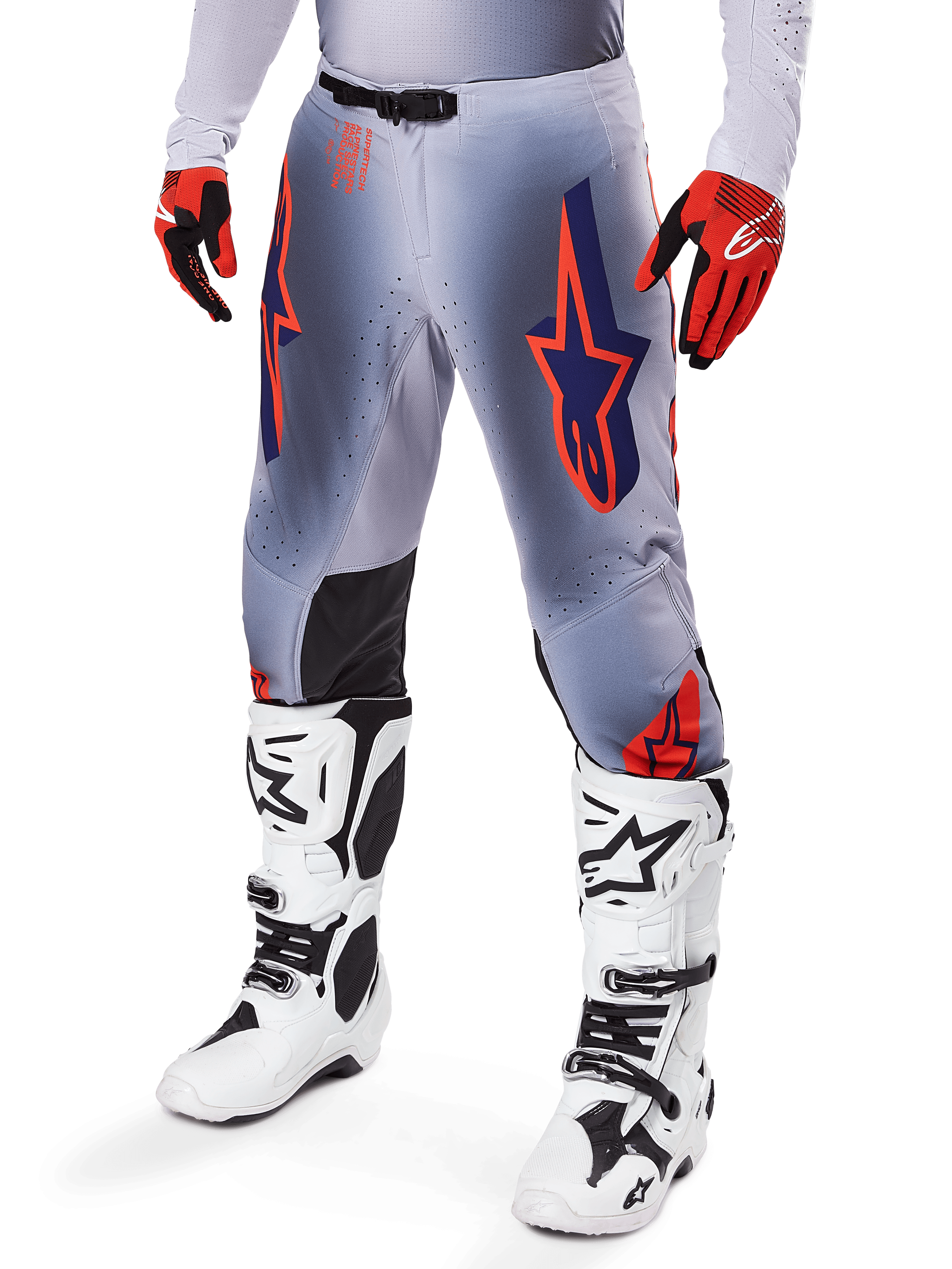 Alpinestars 2025 Supertech Lipan broek, motorcrossbroek, grijs en fluoriserend oranje, met donkerblauwe sterren en zwarte binnenkniepanelen, gedragen met roodoranje handschoenen en witte laarzen, professionele off-road race-uitrusting