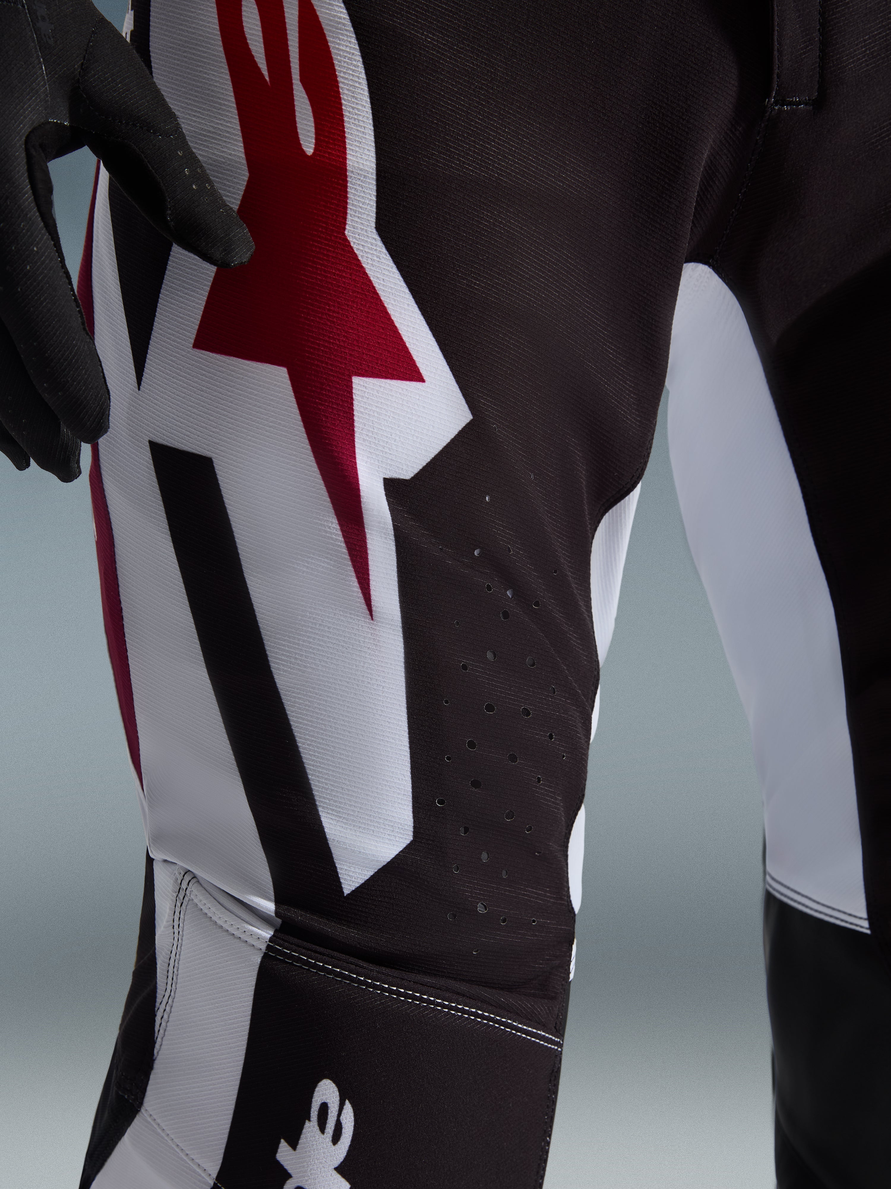 Alpinestars 2026 Supertech AFD Vista Pants, Motocross Pants, Black Red and White, close-up view of the thigh featuring a large red and white Astars logo and laser-cut perforations for ventilation.