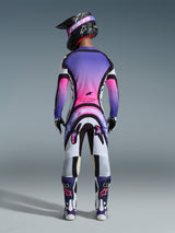 Motocrossrijder van achteren gezien in volledige race-uitrusting, shirt met paars en roze kleurverloop, Alpinestars 2026 Supertech AFD Vista broek in White Purple Black, zwarte helm met paarse crossbril, witte en paarse laarzen, gecoördineerde off-road racekit.