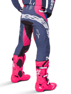 Alpinestars 2025 Techstar Dreem crossbroek, motorcross broek, grijs en roze meerkleurig, achteraanzicht met grote witte Alpinestars-branding op het zitvlak, gedragen met bijpassende felroze Tech 10-laarzen, duurzame off-road race-uitrusting met versterkte panelen.