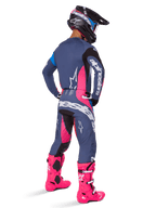 Motorcrossrijder van achteren gezien die een Alpinestars 2025 Techstar Dreem broek draagt, grijsblauw en magenta roze ontwerp met zwarte accenten, gedragen met een bijpassende jersey en felroze laarzen, atletische racepasvorm voor off-road prestaties.