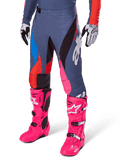 Alpinestars 2025 Techstar Dreem broek, motorcrossbroek, donkergrijs met blauwe, rode en roze panelen, witte graphics, gedragen met felroze laarzen en zwart-witte handschoenen, opvallend high-visibility ontwerp