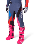 Alpinestars 2025 Techstar Dreem broek, motorcrossbroek, donkergrijs met blauwe, rode en roze panelen, witte graphics, gedragen met felroze laarzen en zwart-witte handschoenen, opvallend high-visibility ontwerp