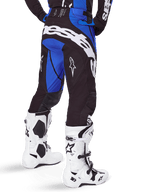 Alpinestars 2025 Techstar Dreem broek, motorcross broek, zwart en blauw, achteraanzicht met opvallende witte Alpinestars-branding op het zitvlak, gedragen met witte en zwarte motorcrosslaarzen en bijpassende blauwe jersey, sportieve pasvorm voor off-road racing
