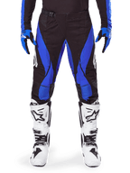 Alpinestars 2025 Techstar Dreem crossbroek, motorcross broek, zwart met blauw, gedragen met bijpassende jersey, handschoenen en witte laarzen, voorzien van blauwe zijpanelen en atletische racepasvorm, duurzaam materiaal voor off-road racen