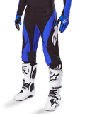 Alpinestars 2025 Techstar Dreem motorcrossbroek, zwart en blauw, gedragen met witte motorcrosslaarzen en blauwe handschoenen, met een wit Alpinestars-logo op de broekspijp, duurzame constructie voor off-road racen