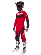 Motorcrossrijder in volledige race-uitrusting met de Alpinestars 2025 Techstar Dreem broek in felrood en zwart, bijpassend rood en zwart jersey met wit logo, zwarte helm en wit-zwarte laarzen, gecoördineerde outfit voor off-road racen.