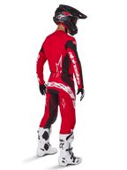 Alpinestars 2025 Techstar Dreem crossbroek, motorcross broek, felrood en zwart, gedragen door een rijder van achteren gezien in een volledige race-uitrusting met bijpassende rode jersey, zwarte helm en witte laarzen, opvallende witte Alpinestars-branding en zwarte stretchpanelen