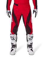 Alpinestars 2025 Techstar Dreem crossbroek, motorcross broek, helderrood en zwart, met hoekige patronen en lasergesneden ventilatiegaten, gedragen met witte motorcrosslaarzen en bijpassende handschoenen voor off-road racing