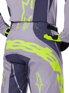 Alpinestars 2025 Techstar Dreem crossbroek, motorcross broek, grijs en donkergrijs met fluorescerende gele accenten, achteraanzicht met opvallende Alpinestars-branding op het achterpand, gedragen met bijpassende jersey en handschoenen, ontworpen voor off-road racing.