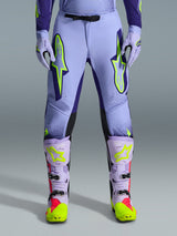 Alpinestars 2026 Supertech Scenz crossbroek, motorcrossbroek, paars geel fluo, met grote neongele logo's op de dijen, gedragen met bijpassende paarse en gele motorcrosslaarzen en handschoenen, atletische performance-pasvorm voor off-road racing