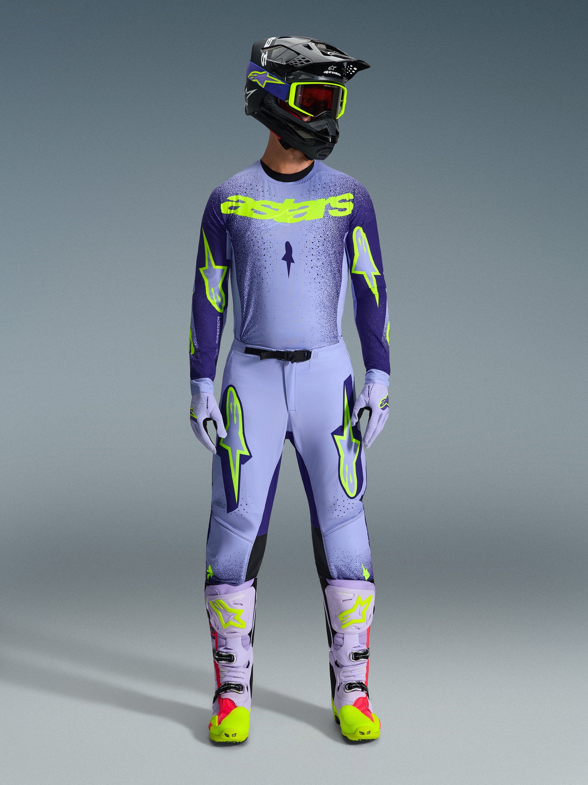Alpinestars 2026 Supertech Scenz broek, motorcross broek, Purple Yellow Fluo, gedragen als een complete race-uitrusting met bijpassende lavendel jersey, handschoenen en laarzen, voorzien van opvallende geel fluo logo's, atletische pasvorm voor professionele off-road racing.