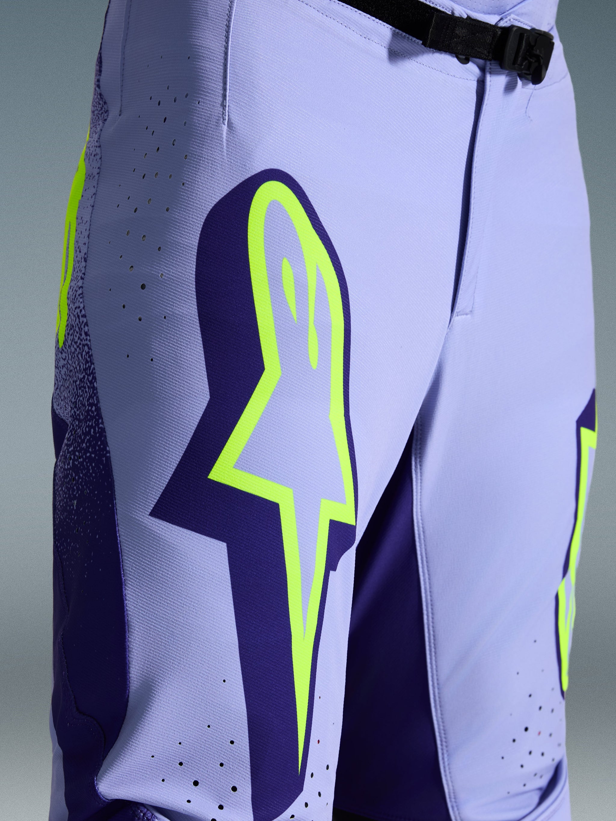 Alpinestars 2026 Supertech Scenz crossbroek, motorcross broek, paars met fluogeel, close-up met groot geel logo op de dij, lasergesneden perforaties voor ventilatie en magnetische gesp bij de taille, sportieve off-road uitrusting