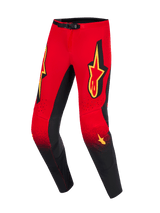 Alpinestars 2026 Supertech Scenz broek, motocrossbroek, rood, zwart en geel, rood bovendeel overgaand in zwarte onderbenen met gespikkeld kleurverloop, grote gele Alpinestars-logo's op de dijen, zwarte kniepanelen aan de binnenzijde en magnetische taillesluiting