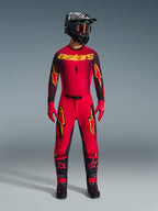 Alpinestars 2026 Supertech Scenz Pants, Motocross Pants, Red Black and Yellow, worn by a rider in a complete racing gear set, matching red and black jersey with yellow logos, black helmet, red gloves, and black boots, athletic pro-fit design for off-road competition