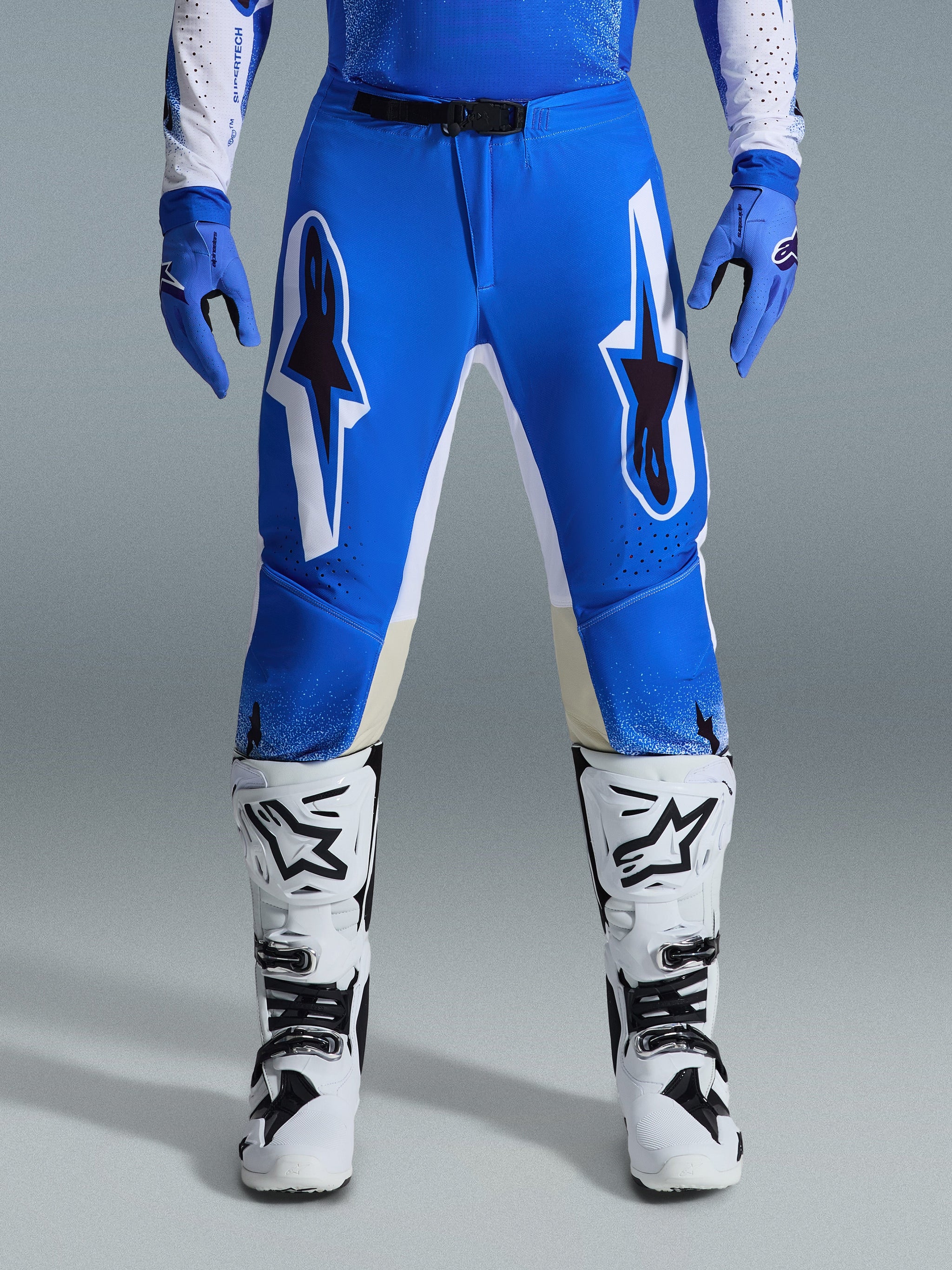 Alpinestars 2026 Supertech Scenz broek, motorcrossbroek, Ucla Blue White, gedragen met bijpassende blauwe handschoenen en witte laarzen, voorzien van grote witte en zwarte graphics op de dijbenen, atletische pasvorm voor off-road prestaties