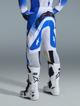 Alpinestars 2026 Supertech Scenz broek, motorcrossbroek, Ucla blauw en wit, achteraanzicht met groot zwart Astars-logo op het zitvlak en 'SUPERTECH'-branding, gedragen met witte Tech 10 laarzen en een bijpassende blauw-witte jersey.