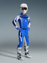 Motorcrosser in volledige race-uitrusting, met de 2026 Supertech Scenz-broek in Ucla Blue en wit, bijpassend blauw-wit shirt met Astars-logo, witte helm met rode crossbril en witte en zwarte laarzen, gecoördineerde outfit voor professioneel off-road racen.