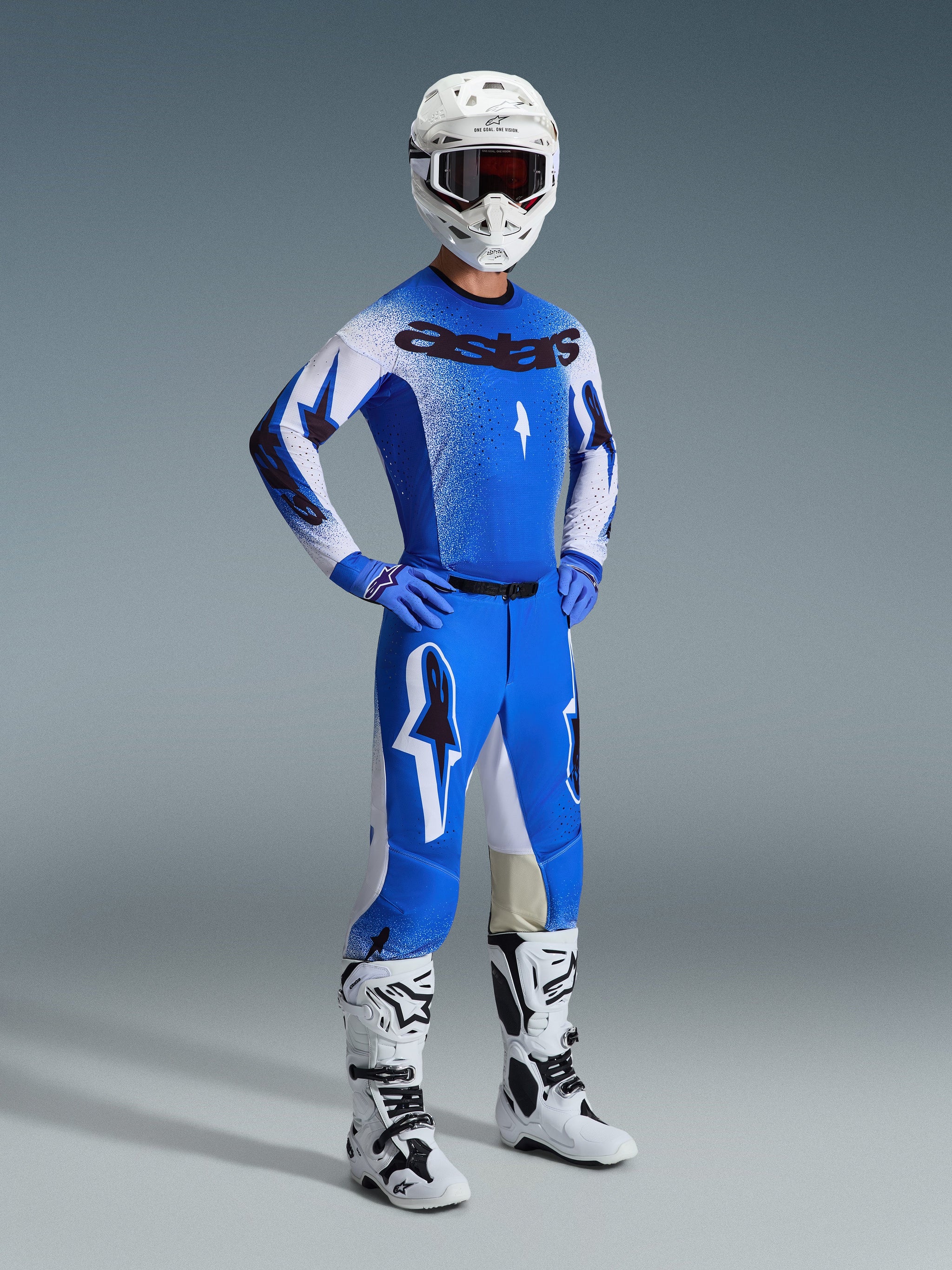 Motorcrosser in volledige race-uitrusting, met de 2026 Supertech Scenz-broek in Ucla Blue en wit, bijpassend blauw-wit shirt met Astars-logo, witte helm met rode crossbril en witte en zwarte laarzen, gecoördineerde outfit voor professioneel off-road racen.