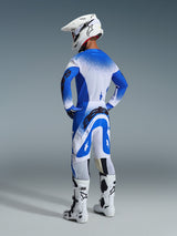 Motorcrosser vanaf de achterzijde in de 2026 Supertech Scenz broek en jersey in Ucla Blue White, witte helm met Alpinestars-logo, witte en zwarte motorcrosslaarzen, professionele off-road race-uitrusting.
