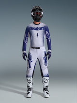 Motorcrossrijder in Alpinestars 2026 Supertech Scenz-kledingset, lichtgrijs en donkerblauw, inclusief jersey en broek met bijpassende blauwe handschoenen, witte en zwarte laarzen, en een zwarte helm met witte crossbril, gecoördineerde outfit voor professionele off-road racing