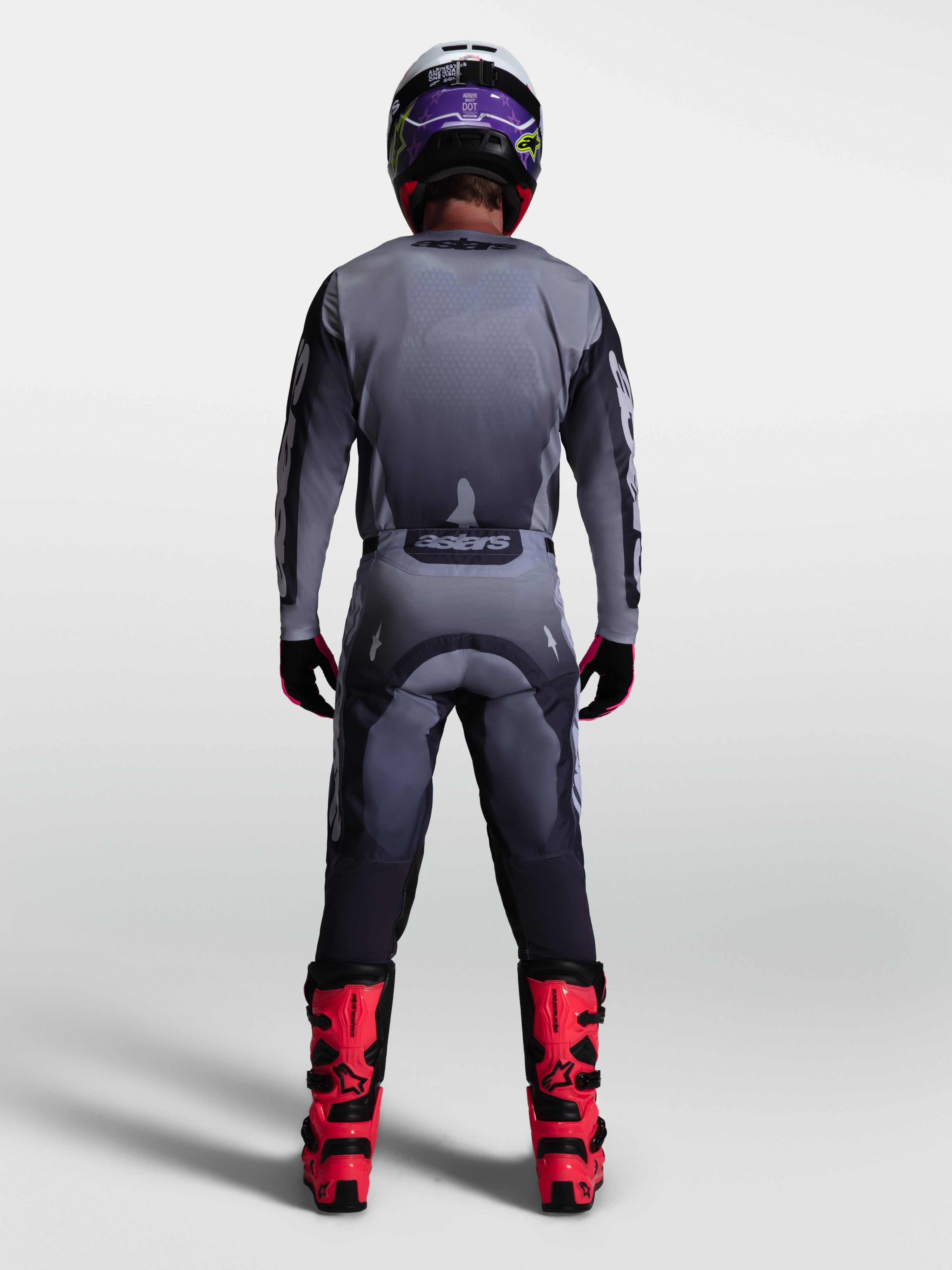 Alpinestars Racer Amber broek, heren motocrossbroek, grijs en licht lila, achteraanzicht met jersey en rode motorlaarzen.