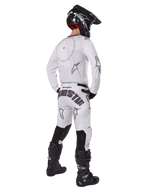 Alpinestars 2025 Racer Hollow Pants, motorcross broek, licht camo bruin en wit, achteraanzicht met opvallende zwarte branding op het zitvlak en sterlogo's, gedragen met bijpassende jersey, zwarte laarzen en een zwarte helm voor een complete off-road racing look