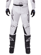 Alpinestars 2025 Racer Hollow crossbroek, motorcrossbroek, licht camo bruin, gedragen met zwarte handschoenen en motorcrosslaarzen, voorzien van een subtiel camouflagepatroon met zwarte grafische prints en Astars-logo's, ergonomisch ontwerp voor off-road rijprestaties
