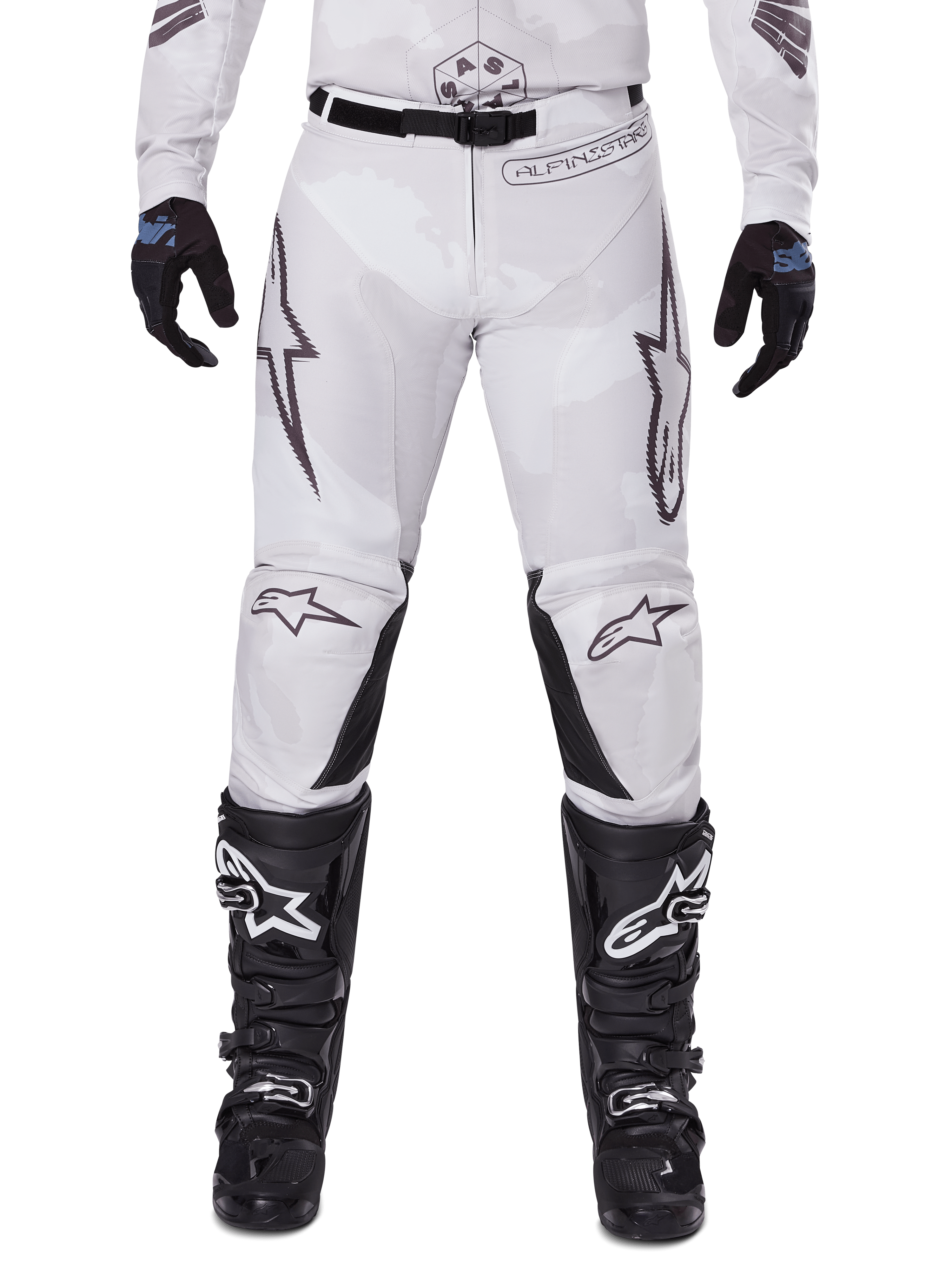Alpinestars 2025 Racer Hollow crossbroek, motorcrossbroek, licht camo bruin, gedragen met zwarte handschoenen en motorcrosslaarzen, voorzien van een subtiel camouflagepatroon met zwarte grafische prints en Astars-logo's, ergonomisch ontwerp voor off-road rijprestaties