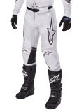 Alpinestars 2025 Racer Hollow Pants, motorcross broek, wit en grijs camo, met grote zwart omijnde sterlogo's en zwarte leren binnenkniepanelen, gedragen met zwarte motorcrosslaarzen en handschoenen, duurzaam ontwerp voor terreinrijden