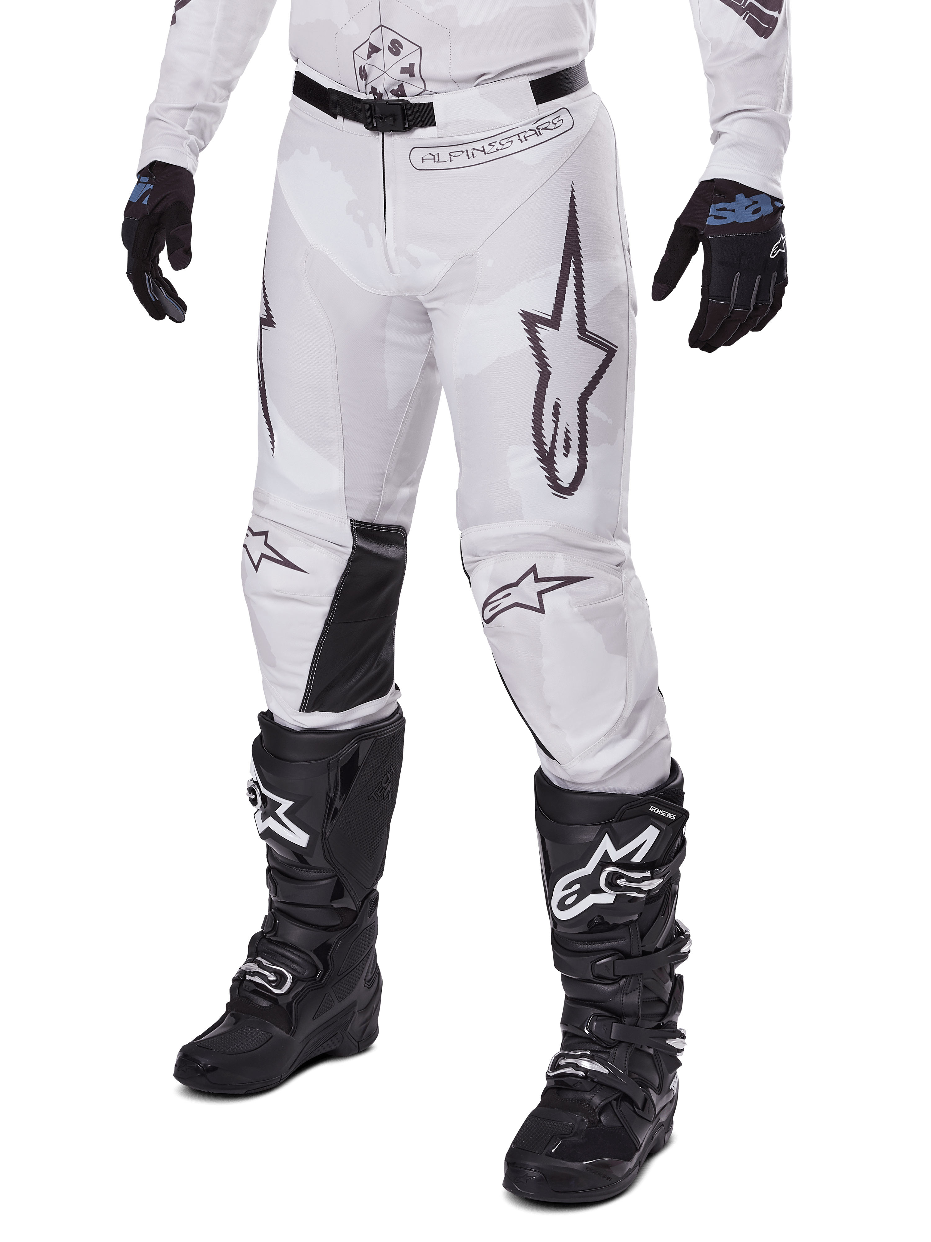 Alpinestars 2025 Racer Hollow Pants, motorcross broek, wit en grijs camo, met grote zwart omijnde sterlogo's en zwarte leren binnenkniepanelen, gedragen met zwarte motorcrosslaarzen en handschoenen, duurzaam ontwerp voor terreinrijden