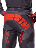 Alpinestars 2025 Racer Hollow broek, motorcrossbroek, Grijs Camo Fluo Oranje, achteraanzicht met groot oranje Alpinestars-logo op het zitvlak, camouflagepatroon met felle oranje accenten, duurzame off-road race-uitrusting