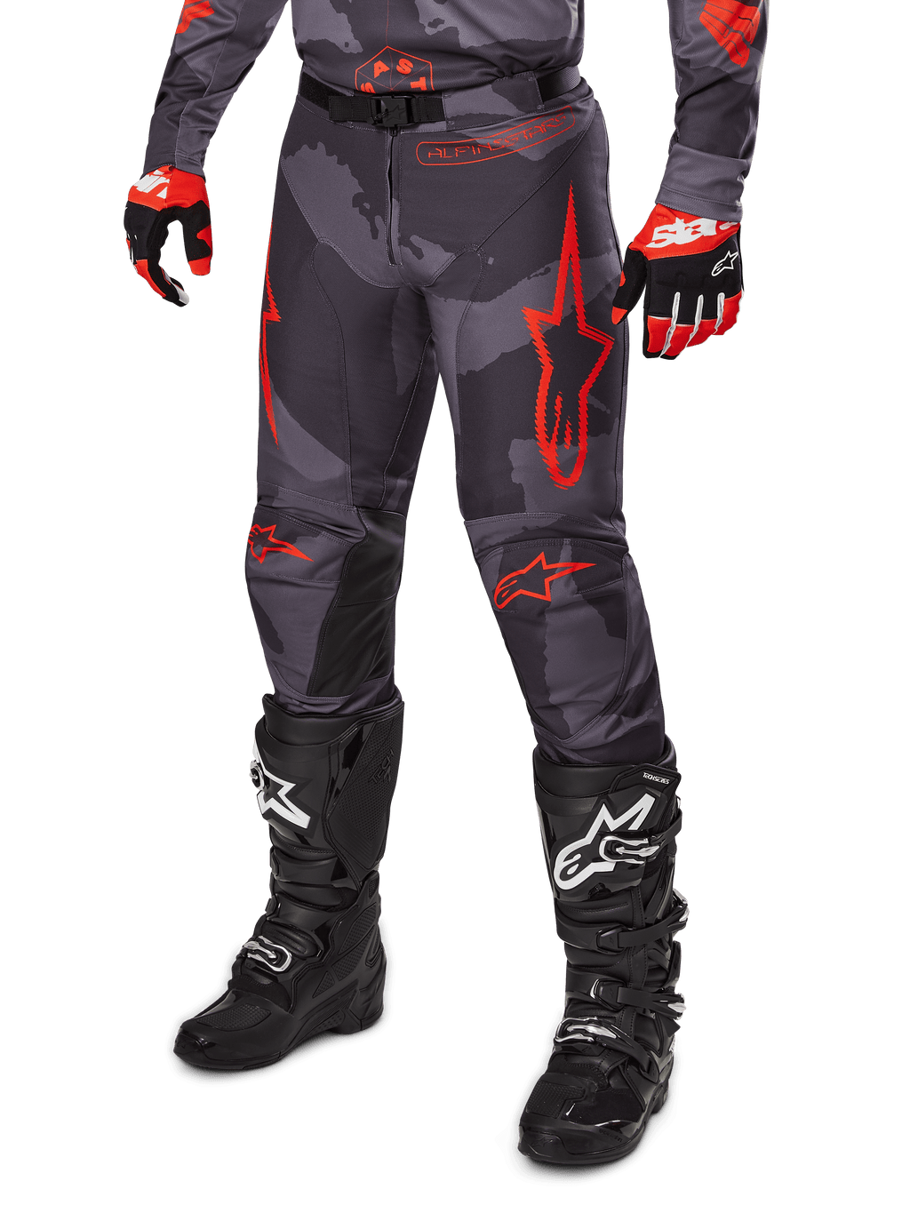 Alpinestars 2025 Racer Hollow broek, motorcrossbroek, grijs camouflage en rood, gedragen met zwarte laarzen en rode handschoenen, voorzien van opvallende rode sterlogo's, camouflagepatroon en duurzame beschermende panelen voor off-road rijden