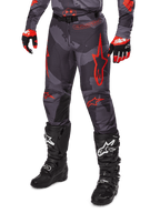 Alpinestars 2025 Racer Hollow broek, motorcrossbroek, grijs camouflage en rood, gedragen met zwarte laarzen en rode handschoenen, voorzien van opvallende rode sterlogo's, camouflagepatroon en duurzame beschermende panelen voor off-road rijden