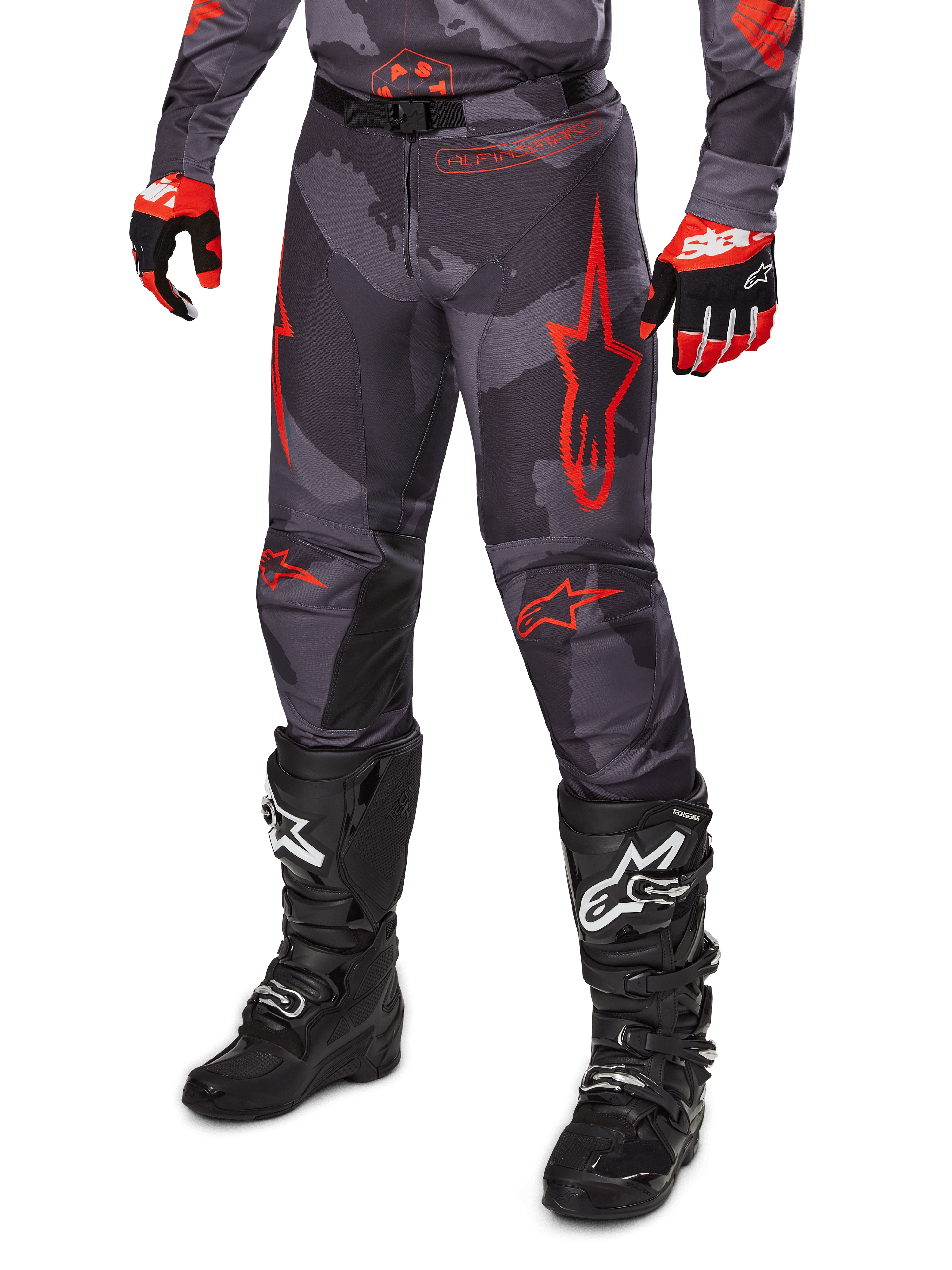 Alpinestars 2025 Racer Hollow broek, motorcrossbroek, grijs camouflage en rood, gedragen met zwarte laarzen en rode handschoenen, voorzien van opvallende rode sterlogo's, camouflagepatroon en duurzame beschermende panelen voor off-road rijden