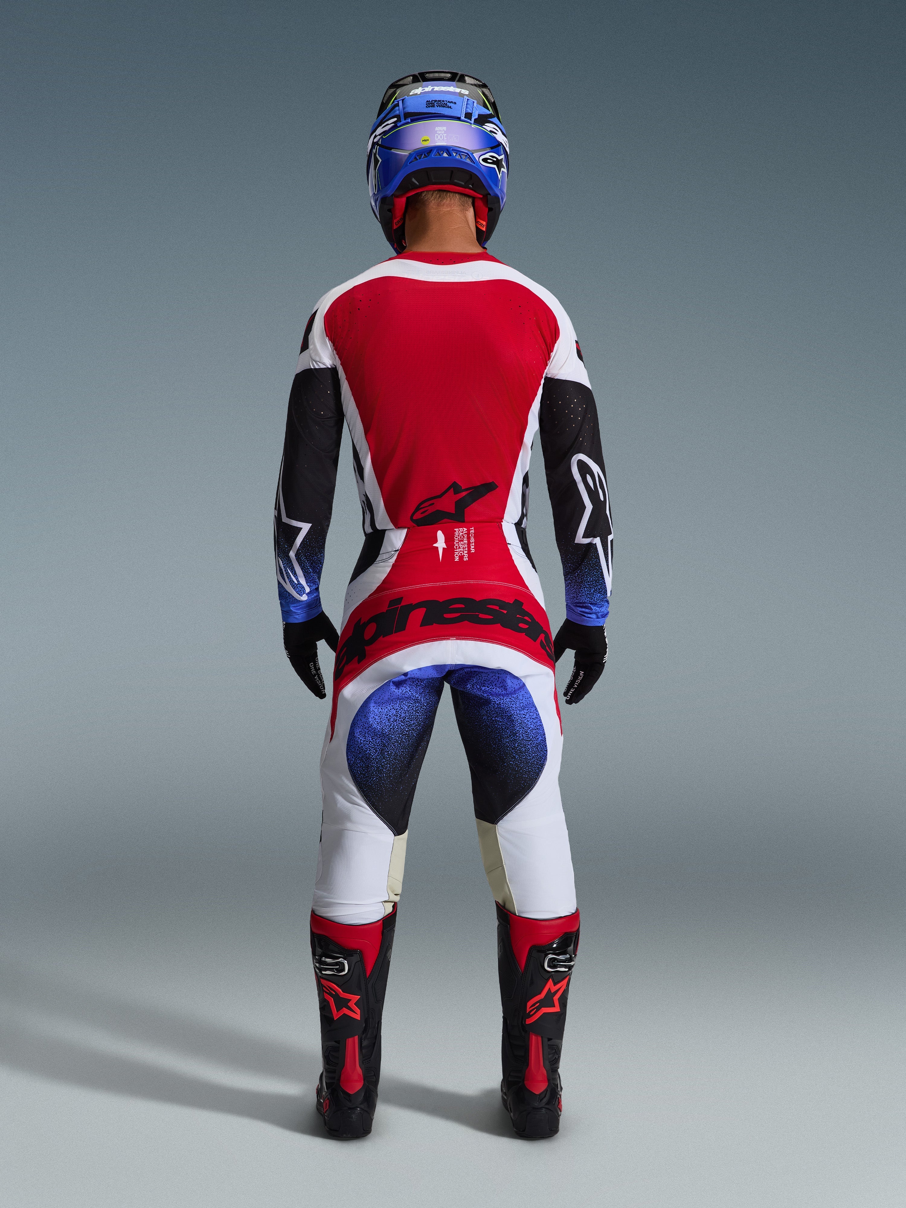Alpinestars 2026 Techstar Knif Pants, Motocross Pants, Black White Red and Blue, back view of a rider in complete gear including matching jersey, blue helmet, and black and red boots, featuring bold Alpinestars branding on the seat.