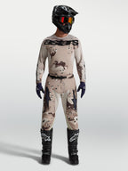Alpinestars Racer Lone broek en jersey, heren motorcross-set in desert camo zwart, gedragen door model met zwarte motorlaarzen en helm, professionele off-road race-uitrusting.