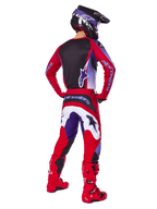 Motorcrosser van achteren gezien in Alpinestars 2025 Fluid Wurx Pants, paars en felrood met witte en zwarte accenten, bijpassende jersey, zwarte helm en rode laarzen, gecoördineerde outfit voor off-road racen