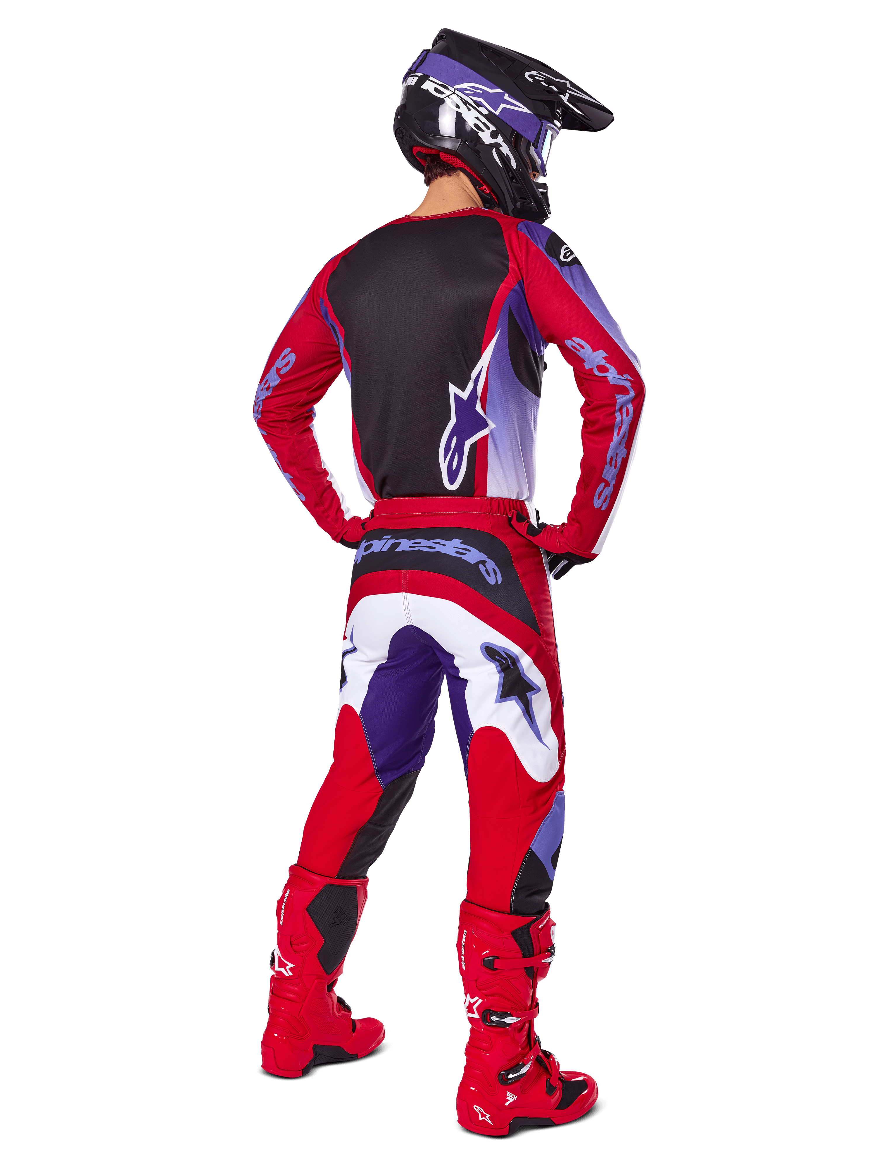 Motorcrosser van achteren gezien in Alpinestars 2025 Fluid Wurx Pants, paars en felrood met witte en zwarte accenten, bijpassende jersey, zwarte helm en rode laarzen, gecoördineerde outfit voor off-road racen