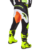 Alpinestars 2025 Fluid Wurx broek, motorcross broek, geel en zwart met oranje en witte accenten, achteraanzicht gedragen met bijpassende felgele laarzen, duurzame constructie met opvallende branding voor motorcross