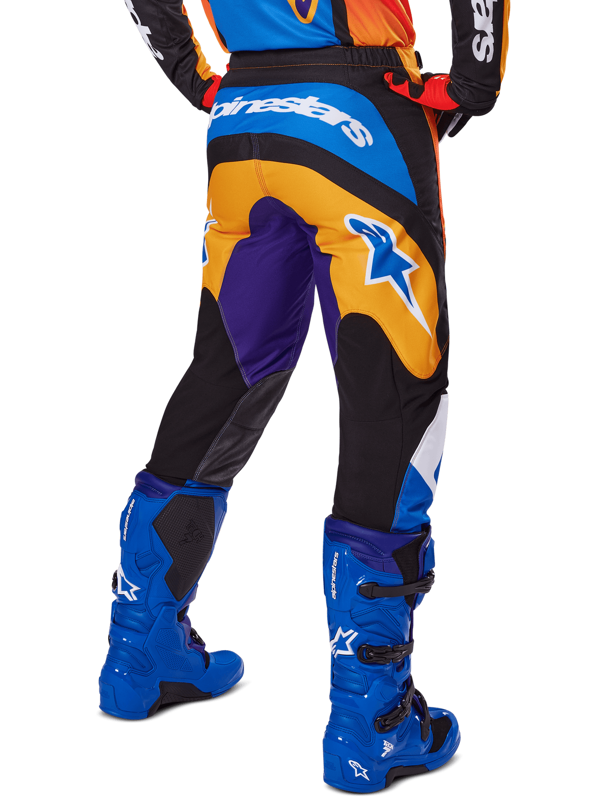 Alpinestars 2025 Fluid Wurx broek, motorcrossbroek, multicolor met oranje, paars en blauw, achteraanzicht met wit Alpinestars-logo op de achterkant, gecombineerd met blauwe motorcrosslaarzen, sportieve pasvorm voor off-road rijden.