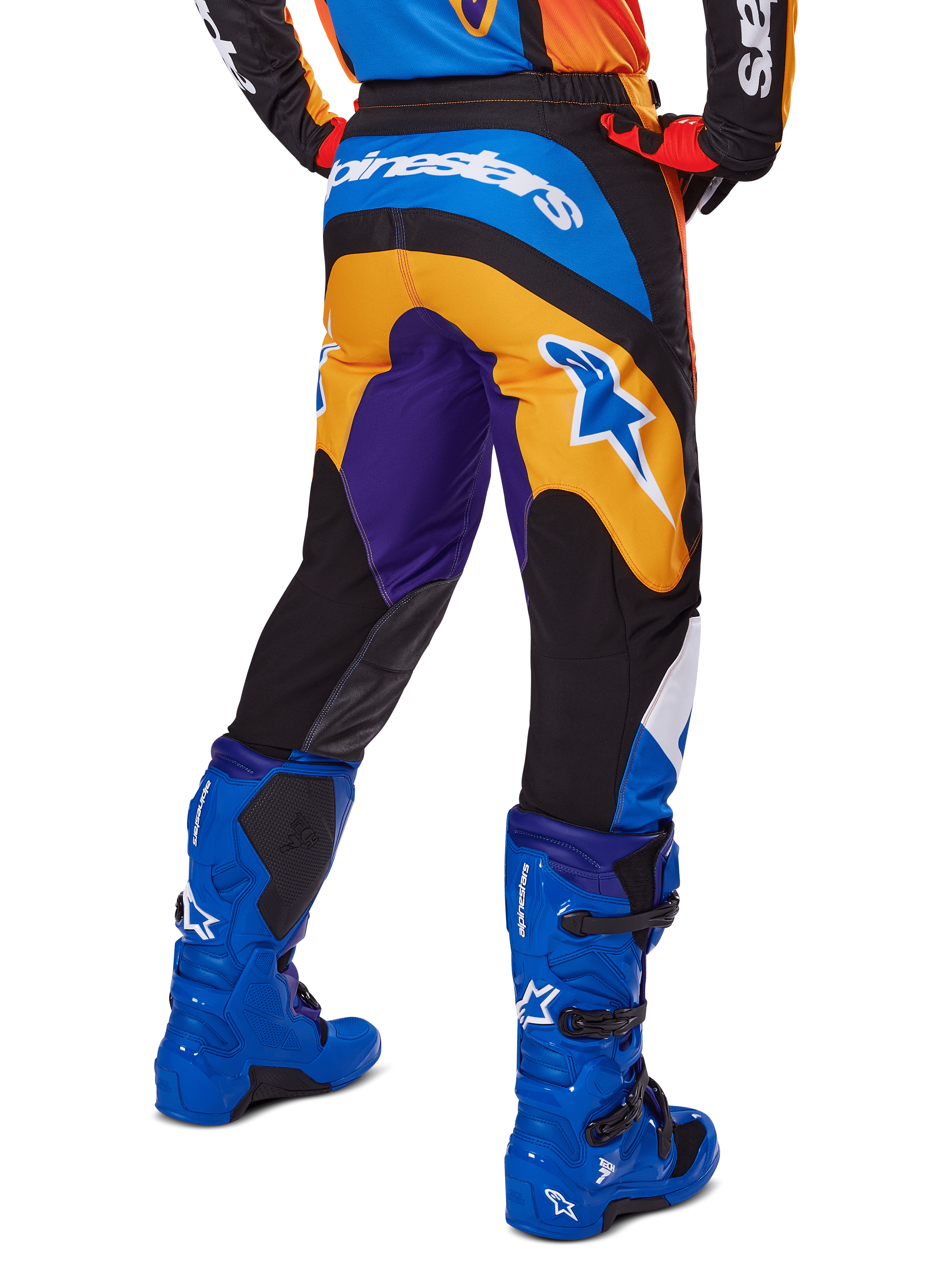 Alpinestars 2025 Fluid Wurx broek, motorcrossbroek, multicolor met oranje, paars en blauw, achteraanzicht met wit Alpinestars-logo op de achterkant, gecombineerd met blauwe motorcrosslaarzen, sportieve pasvorm voor off-road rijden.