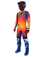 Motorcrosser in volledige race-uitrusting, Alpinestars 2025 Fluid Wurx broek en bijpassende jersey met een multicolor verloop van oranje, rood en paars, zwarte helm met rode crossbril, blauwe en zwarte laarzen, rode en zwarte handschoenen, gecoördineerde outfit voor off-road racing