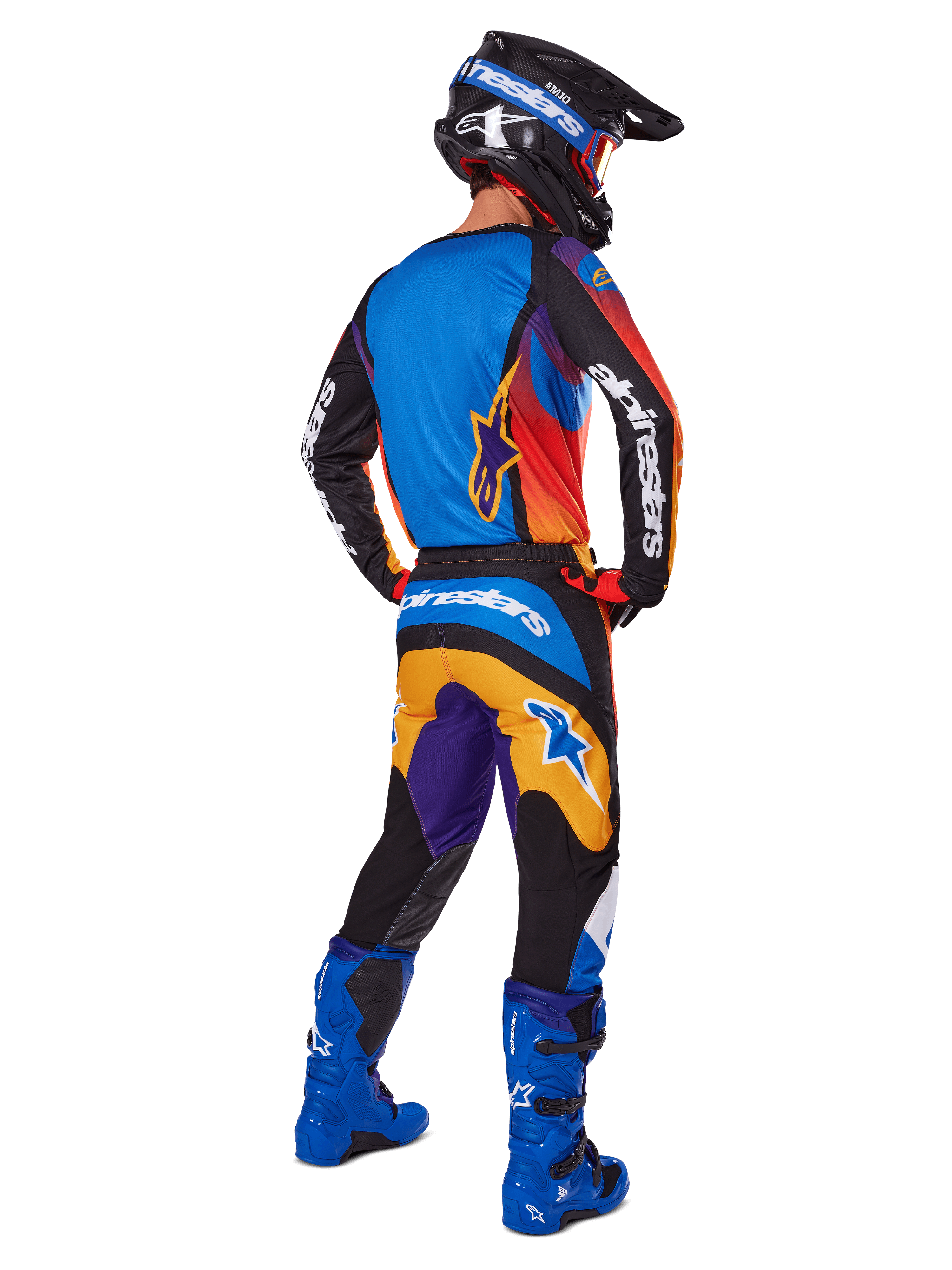 Motorcrosser van achteren gezien, Alpinestars 2025 Fluid Wurx broek, multicolor ontwerp met blauwe, oranje, gele en paarse accenten, gecombineerd met een bijpassende jersey, felblauwe laarzen en zwarte helm, complete off-road race-uitrusting