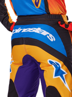 Alpinestars 2025 Fluid Wurx broek, motorcrossbroek, achteraanzicht in oranje, blauw en paars, met een wit Alpinestars-logo op het zitvlak en een blauw Astar-logo op de broekspijp, technische constructie voor off-road rijden