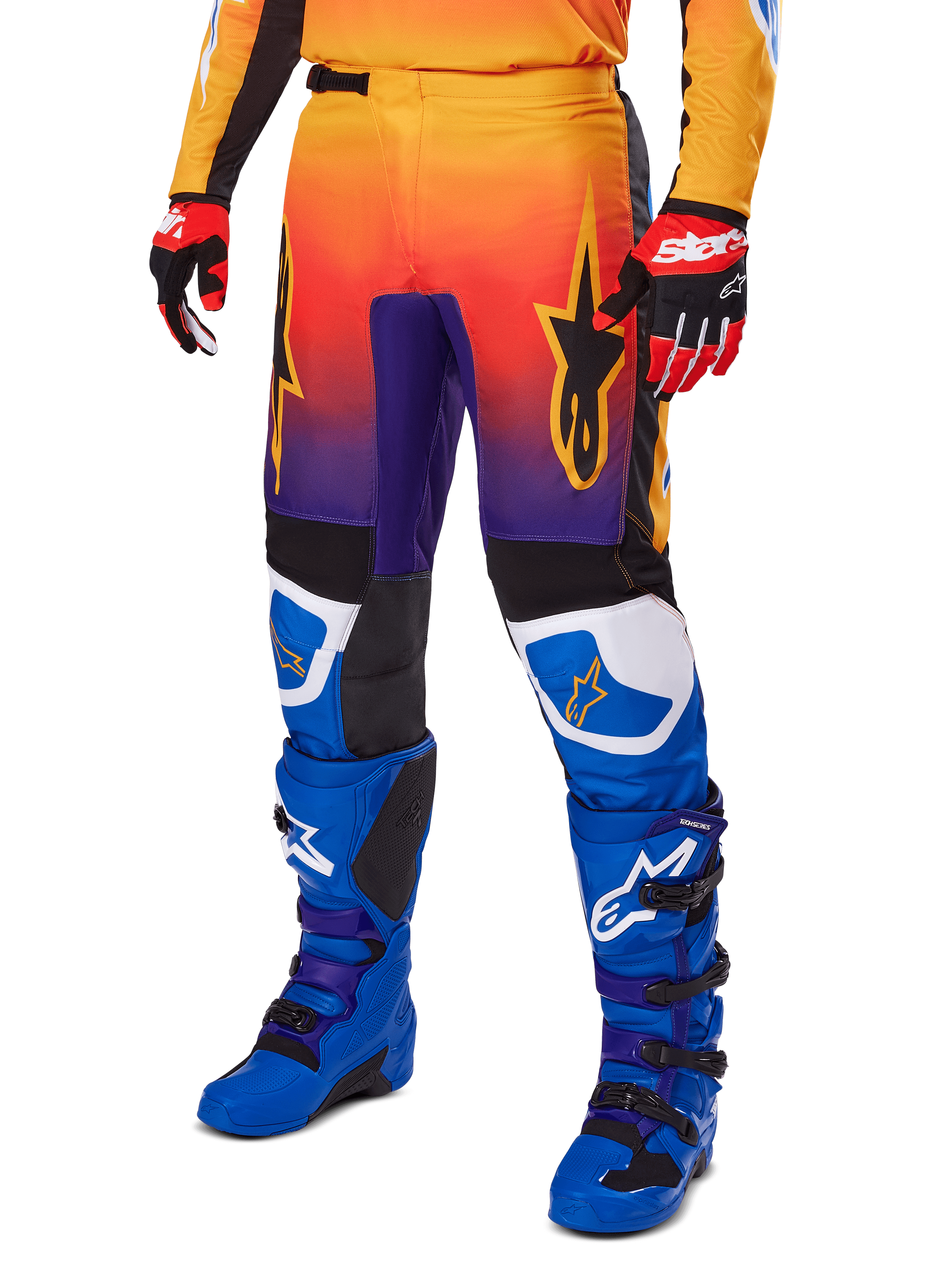 Alpinestars 2025 Fluid Wurx broek, motorcrossbroek, multicolor oranje, rood en paars kleurverloop met zwarte en blauwe panelen, gedragen met blauwe laarzen en rode handschoenen, voorzien van sterlogo-graphics en witte knie-accenten, duurzame prestatiegerichte uitrusting voor off-road racing